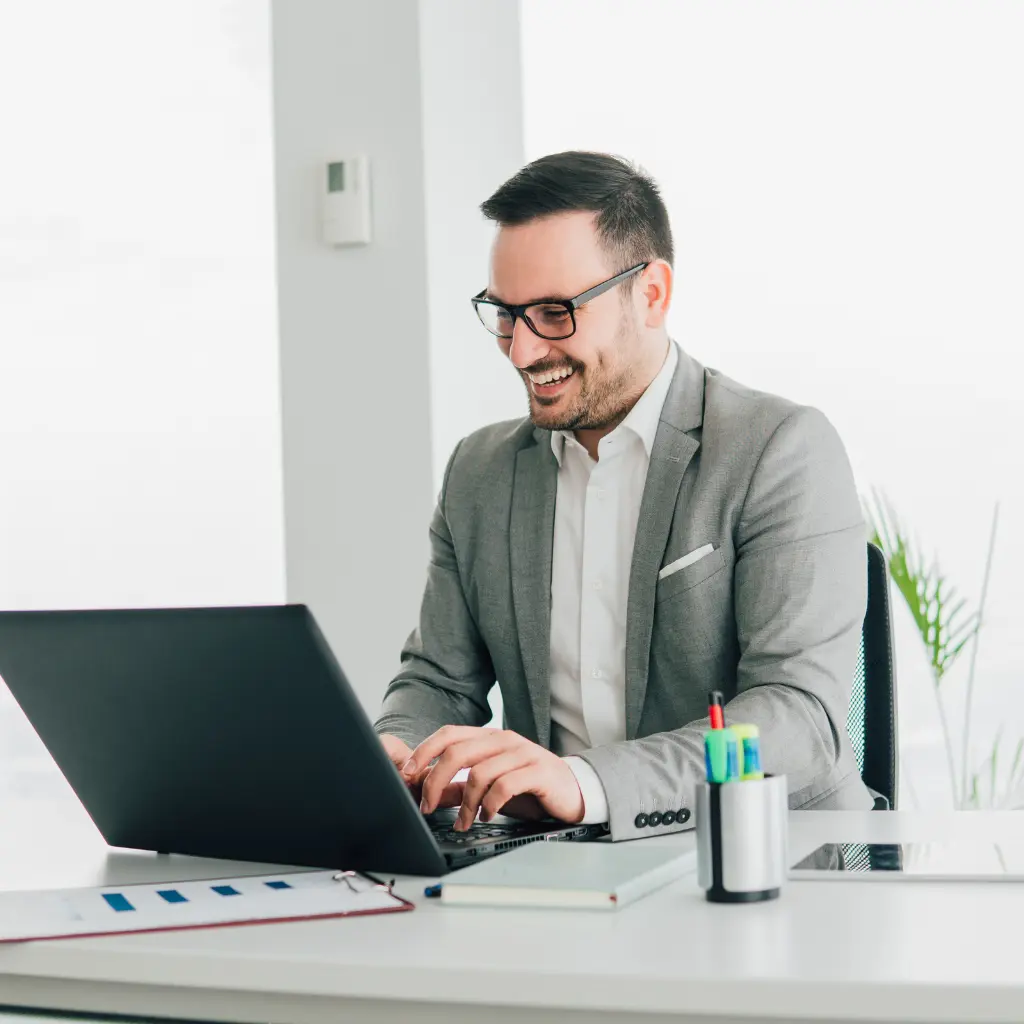 Homme souriant en costume travaillant sur un ordinateur portable dans un bureau professionnel chez Aurore SA